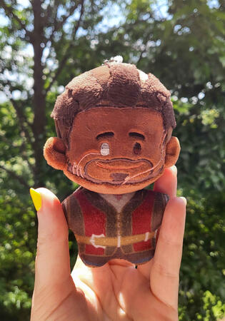Picture of hand holding 10cm Wyll plushie against green foliage